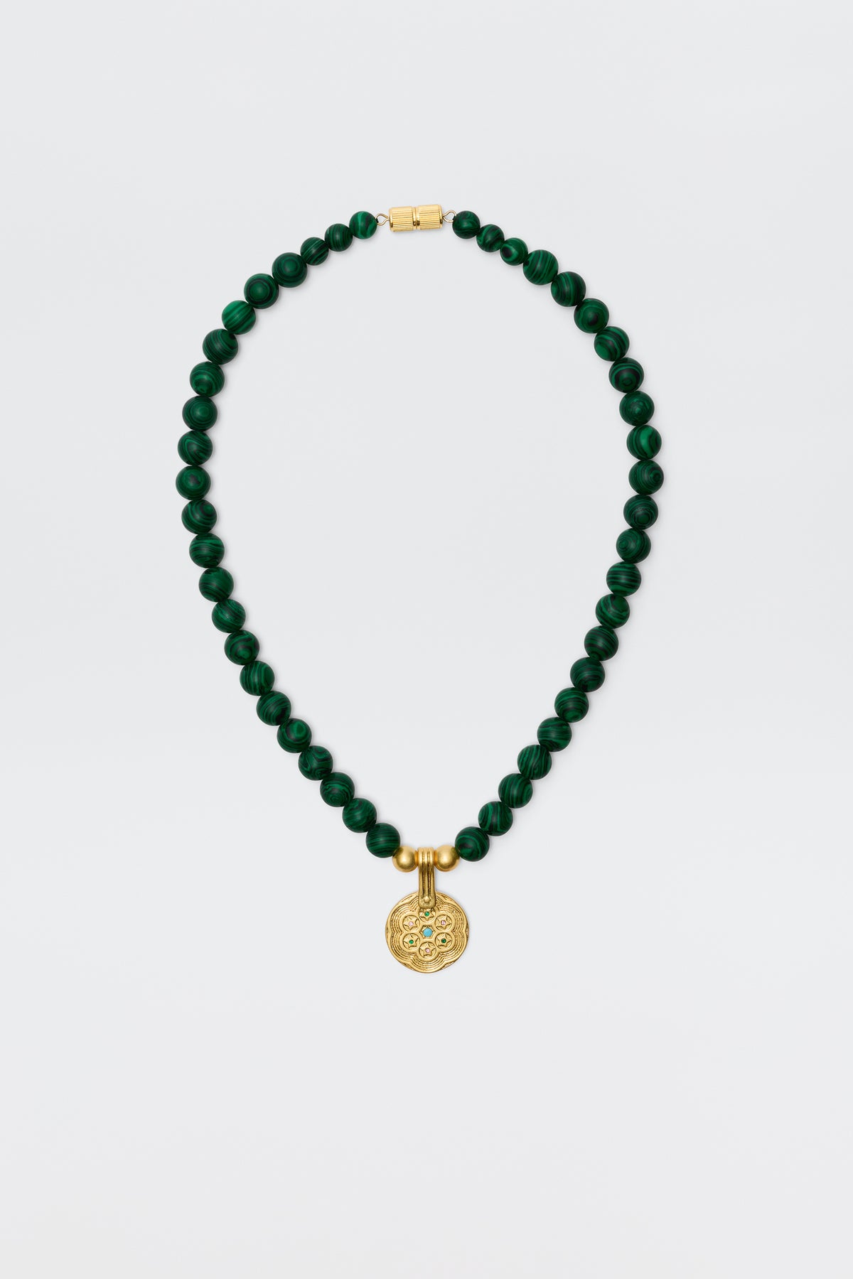 The Ischia - Green necklace features round dark green malachite beads with a gold clasp and an engraved golden pendant, displayed on a plain white background.