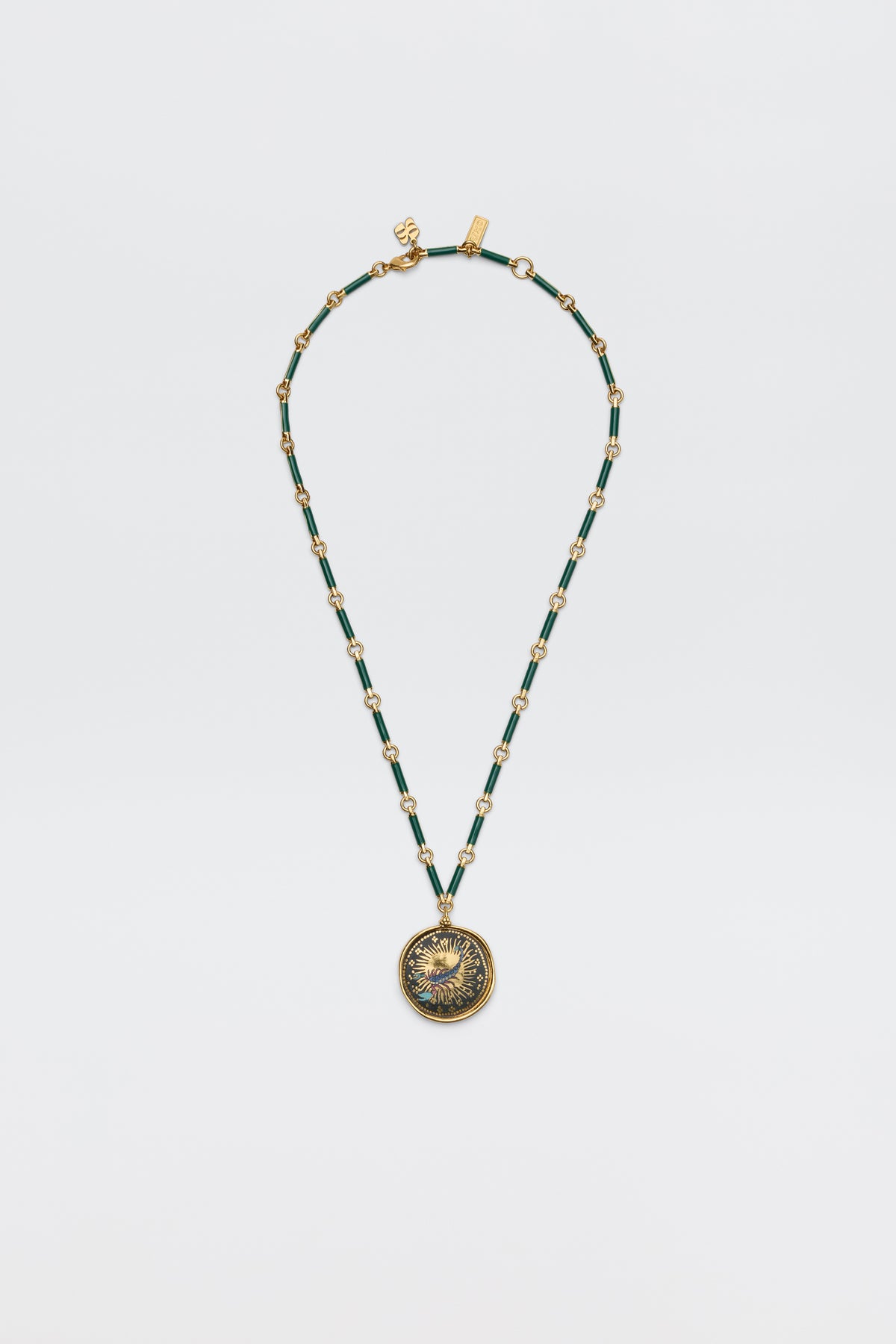 The Ari - Astro Scorpio necklace features gold and green beads with an ornate round pendant bearing an embossed design, displayed elegantly on a plain white background.