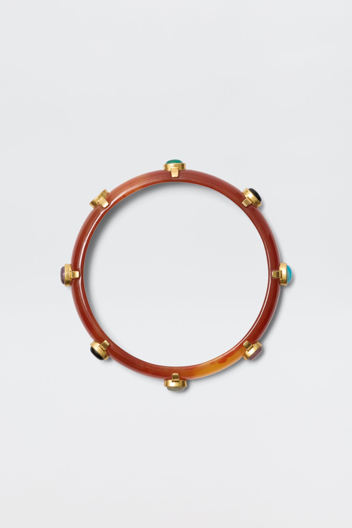The Sabella - Tortoise is a circular resin bangle in brown with gold-plated accents and multicoloured cabochons spaced around it, shown on a plain light grey background.