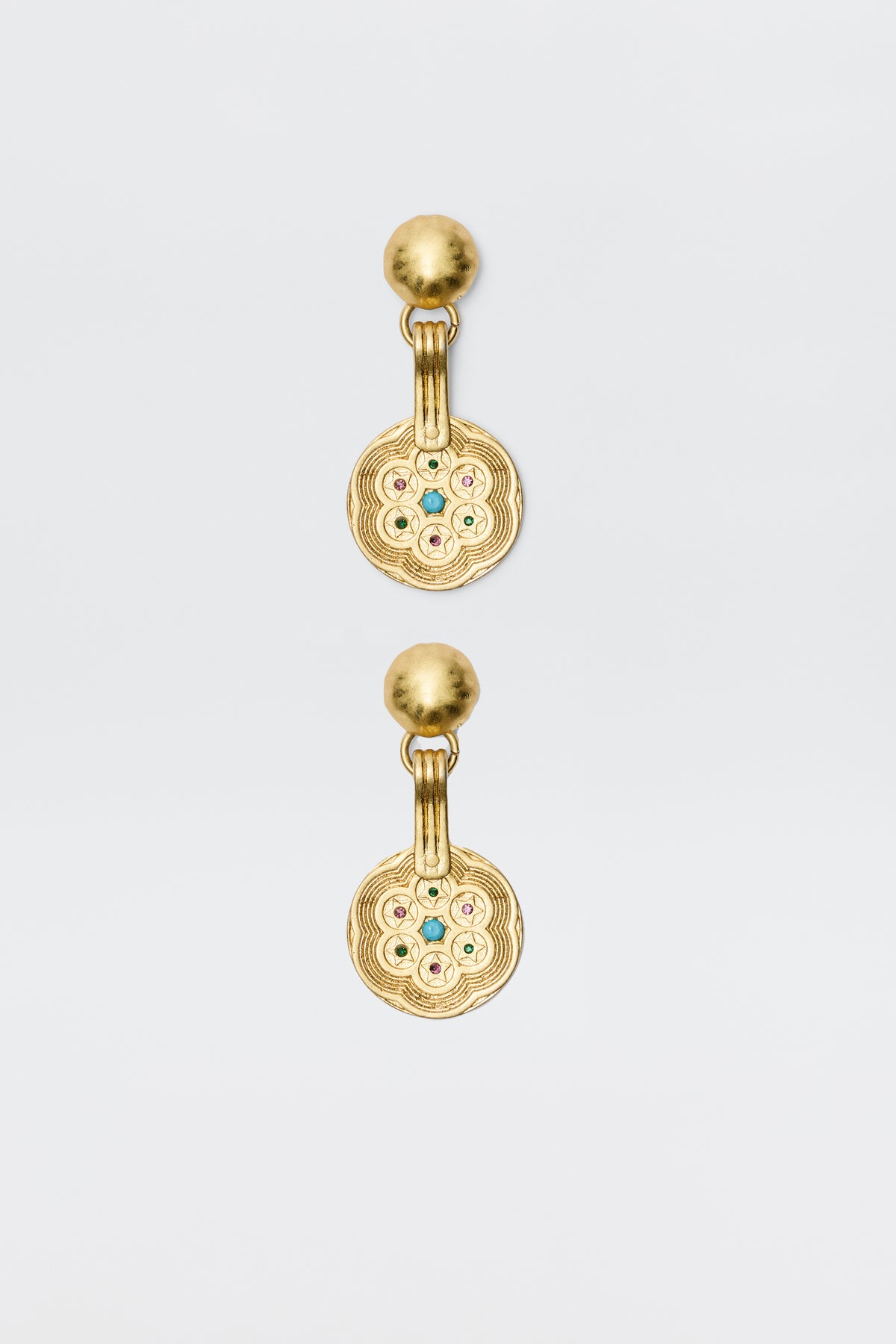 A pair of Anouk - Gold drop earrings with round, textured discs featuring a circular pattern and central colored gemstones, attached to smooth gold studs. Vintage-inspired, photographed on a plain white background.