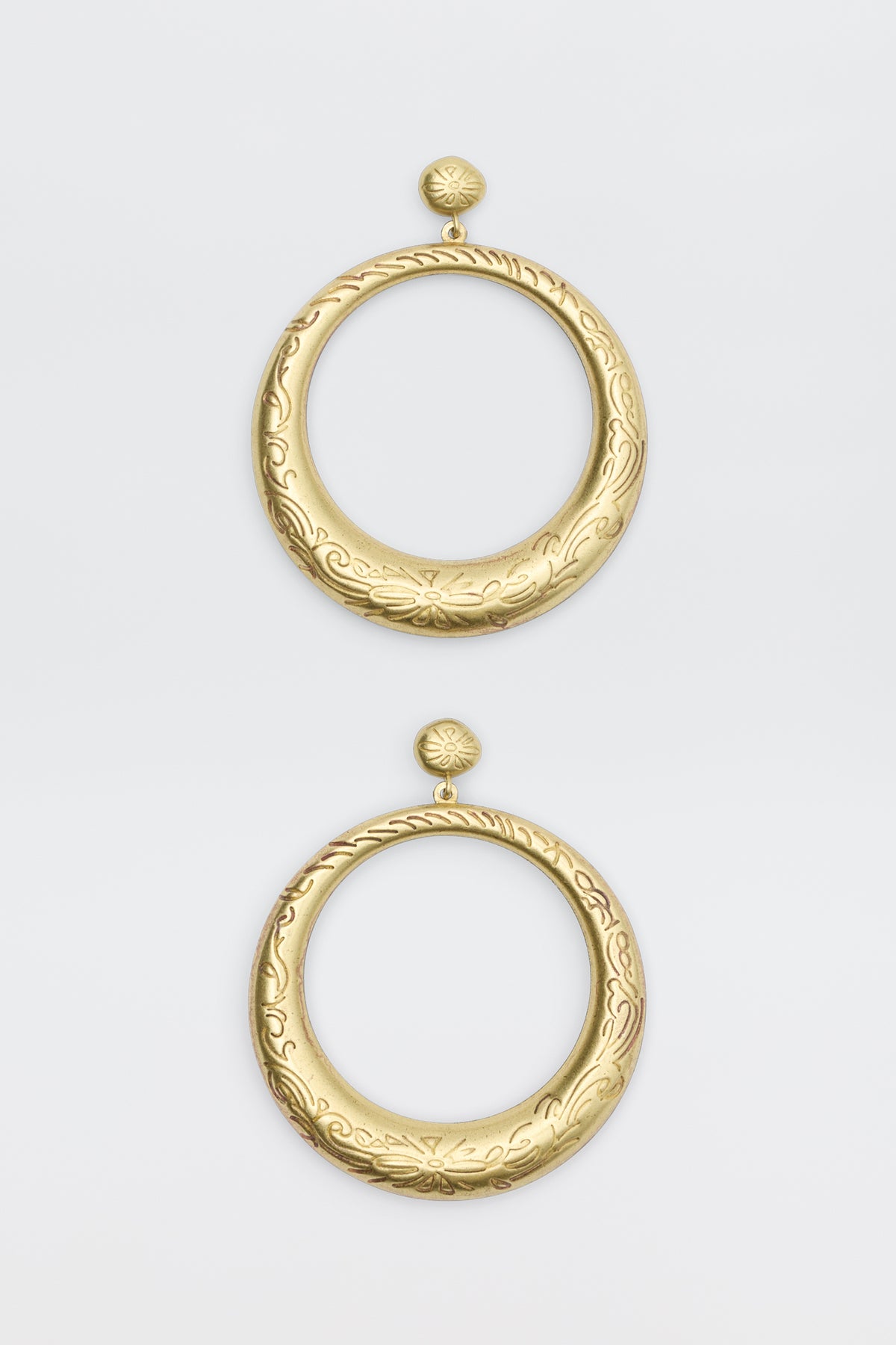The Sian - Gold earrings are large, circular gold hoops with intricate engraved floral and swirl patterns. Each earring features a round stud top connected to a wide open hoop, displayed on a plain white background.