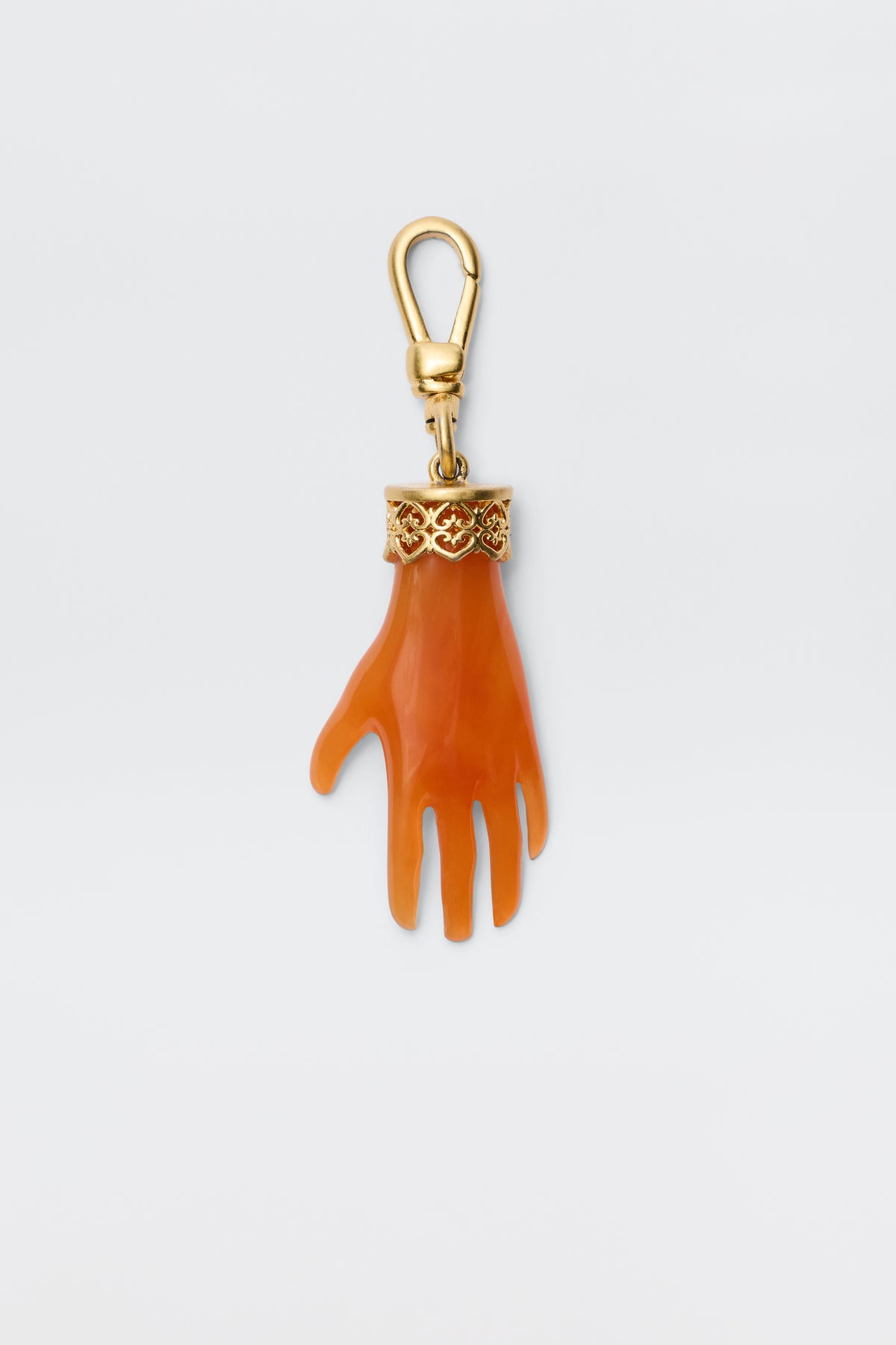 The Hand - Orange keychain features an orange, gold-plated hand charm with a gold ornate band at the wrist, attached to a gold lobster clasp. Shown against a plain white background.