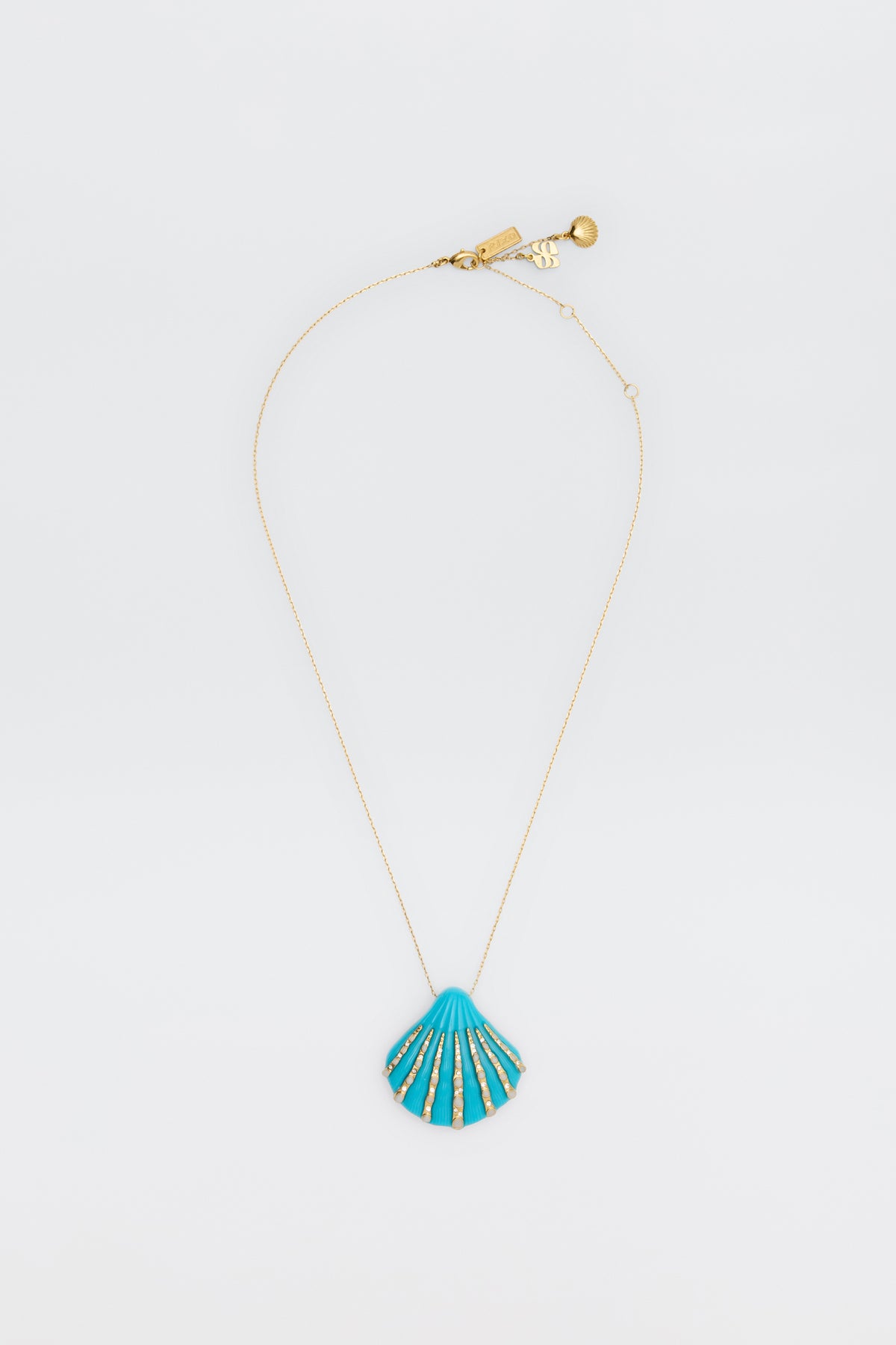 The Leanira - Turquoise necklace features a delicate gold chain with a blue seashell-shaped pendant accented in gold, shown on a plain white background.