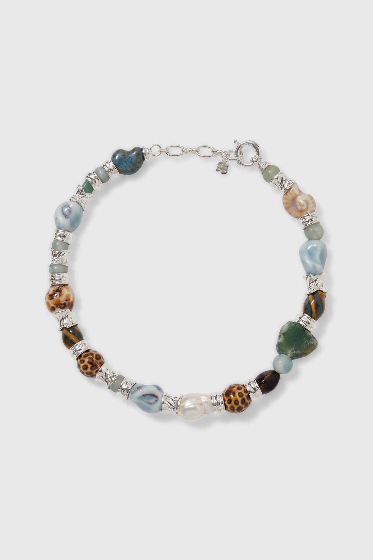 Introducing Maxina - Blue: a beaded necklace featuring multicolored, irregularly shaped stones and silver spacers, finished with a silver clasp. The design showcases beads in animal print, blue, green, pearl, and marbled patterns arranged in a stylish circular layout.