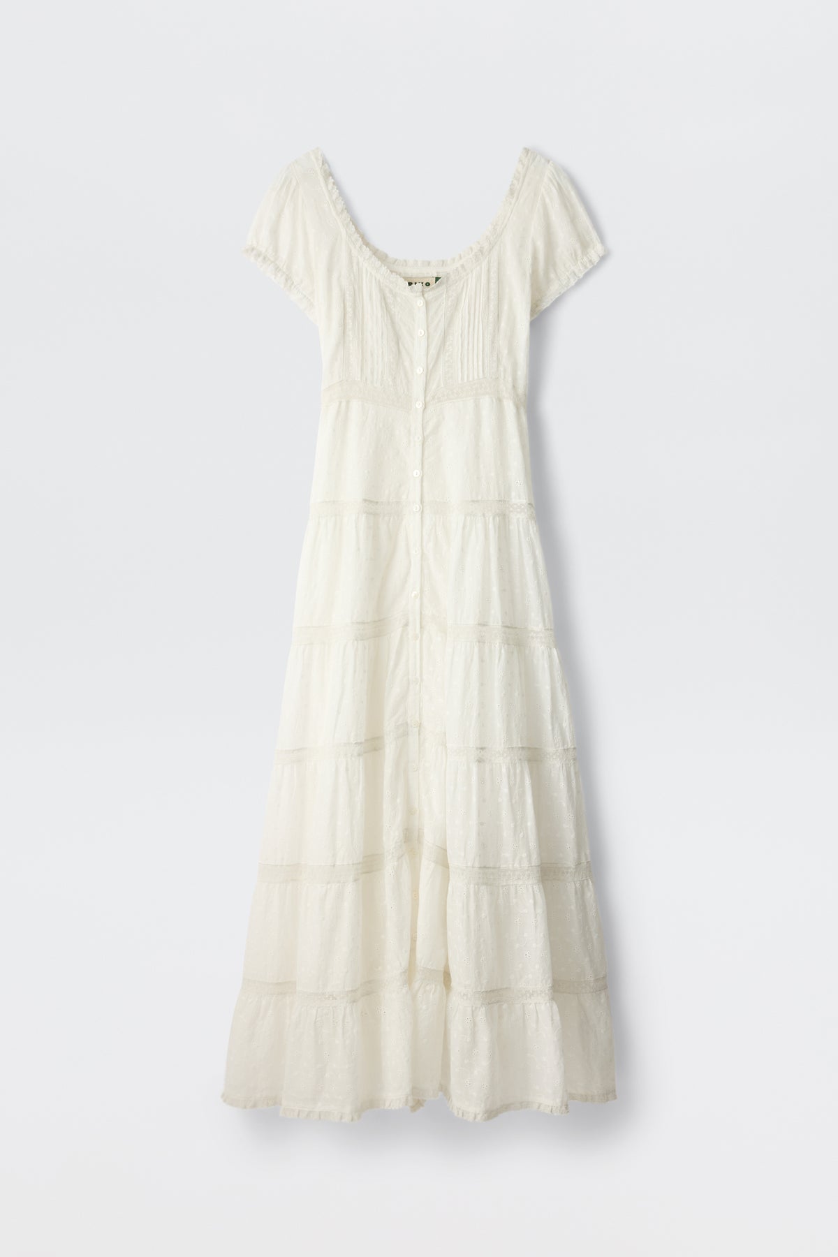 The Jaclyn - Ivory is a white cotton summer dress with short sleeves, an ankle-length tiered skirt, fitted bodice, button-down front, and lace-trimmed neckline and sleeves. The delicate fabric has a textured broderie anglaise pattern.