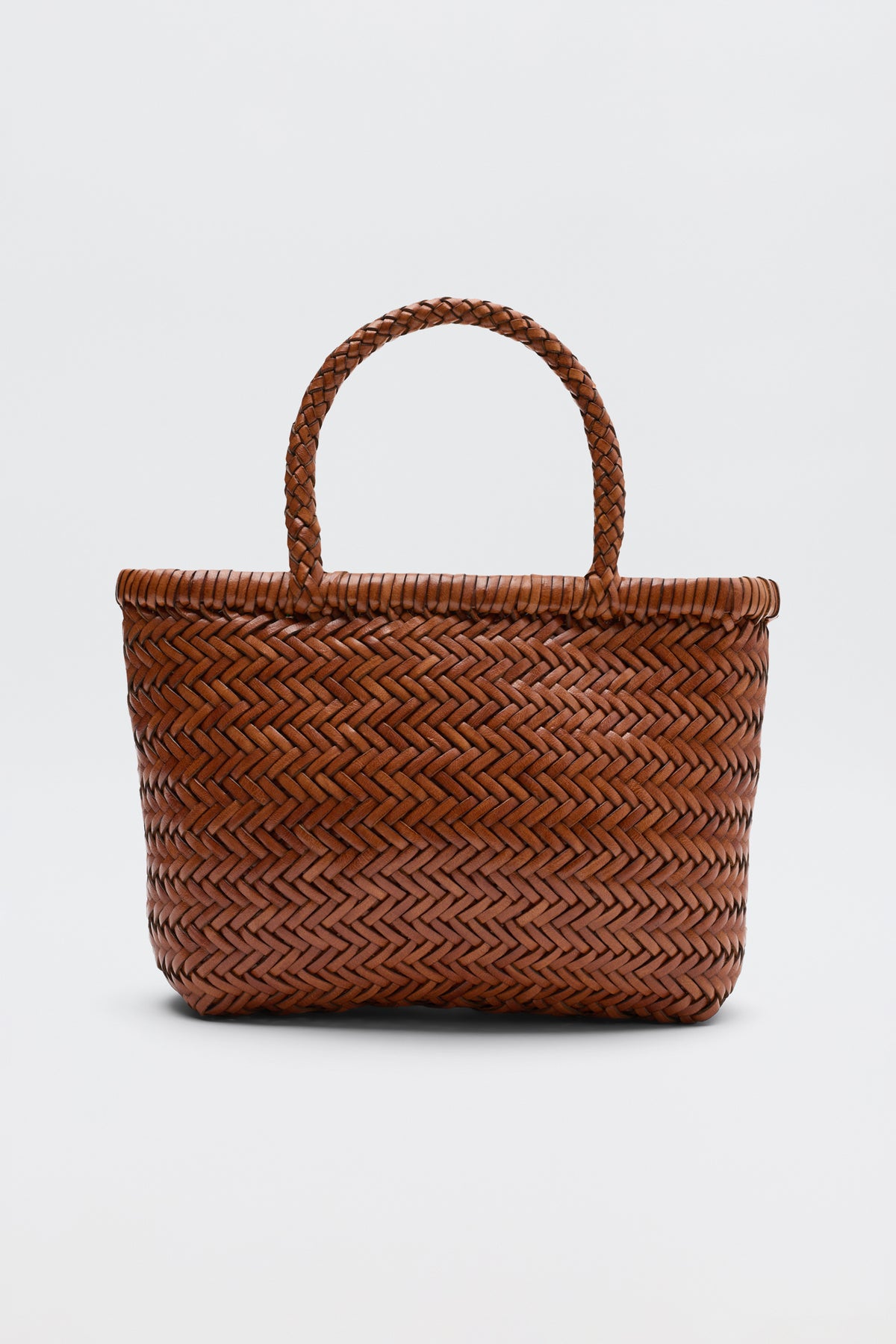 The Lysia - Tan is a brown woven tote bag with two braided handles, reminiscent of vintage woven bags by Dragon Diffusion, displayed against a plain white background.
