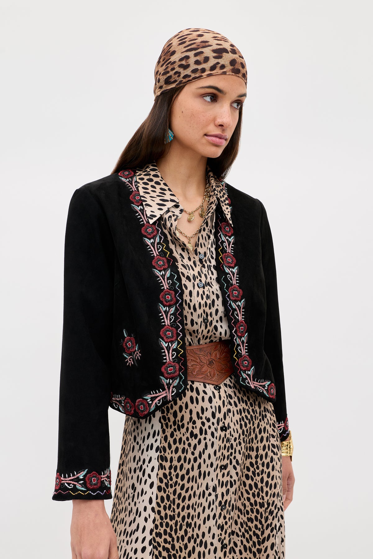 Woman wearing the Oliwia - Roselle Embellishment Black jacket over a leopard print dress and headscarf, styled with a brown belt, green earring, and gold necklace, standing against a plain light background.