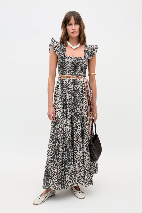 A woman poses against a white background wearing the Kendall - Nina Leopard Mocha dress, styled with a beaded necklace, gold bangles, a brown woven bag, and white slip-on shoes.