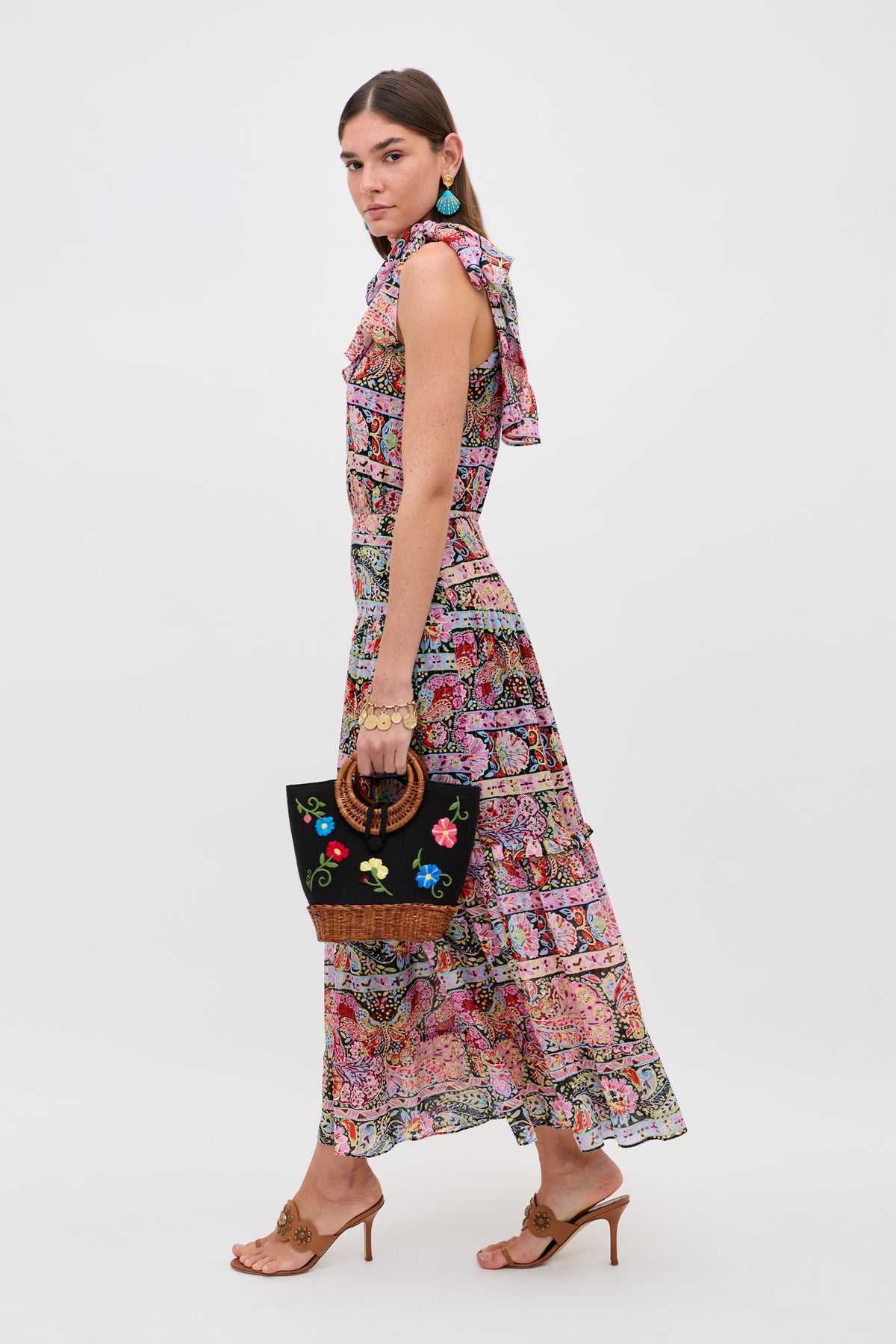 A woman wears the Abi - Cara Stripe Black maxi dress, styled with tan heeled sandals, turquoise earrings, and a black floral embroidered handbag, standing against a plain white background.