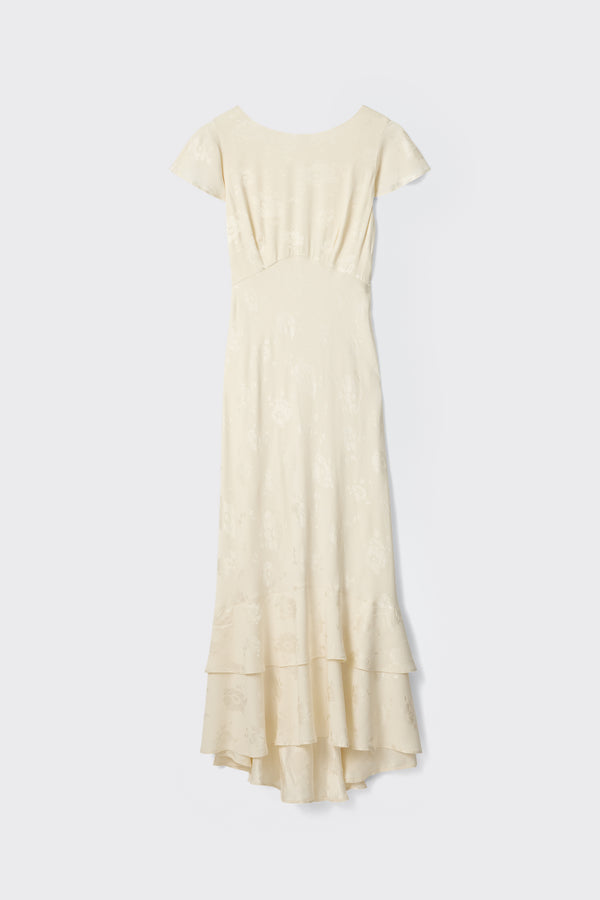 The Liberty - Poppy is a long ivory jacquard dress with cap sleeves, a fitted waist, subtle floral pattern, and tiered ruffled hem, displayed against a plain light background.