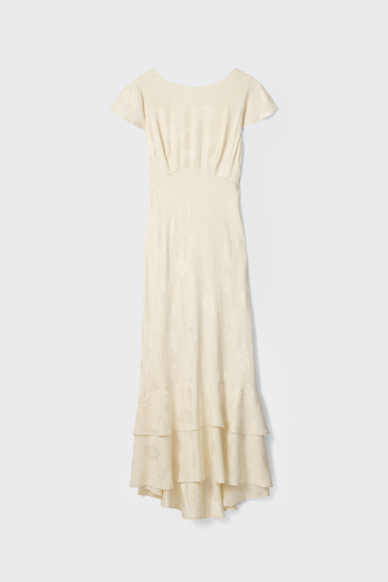 The Liberty - Poppy is a long ivory jacquard dress with cap sleeves, a fitted waist, subtle floral pattern, and tiered ruffled hem, displayed against a plain light background.