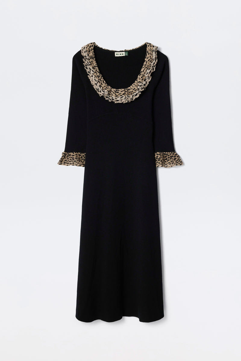 The Mika - Antelope Spot Black is a long-sleeved black scoop neck dress with wide ruffled neckline and sleeve cuffs, featuring a brown and black antelope spot print, displayed on a plain white background.