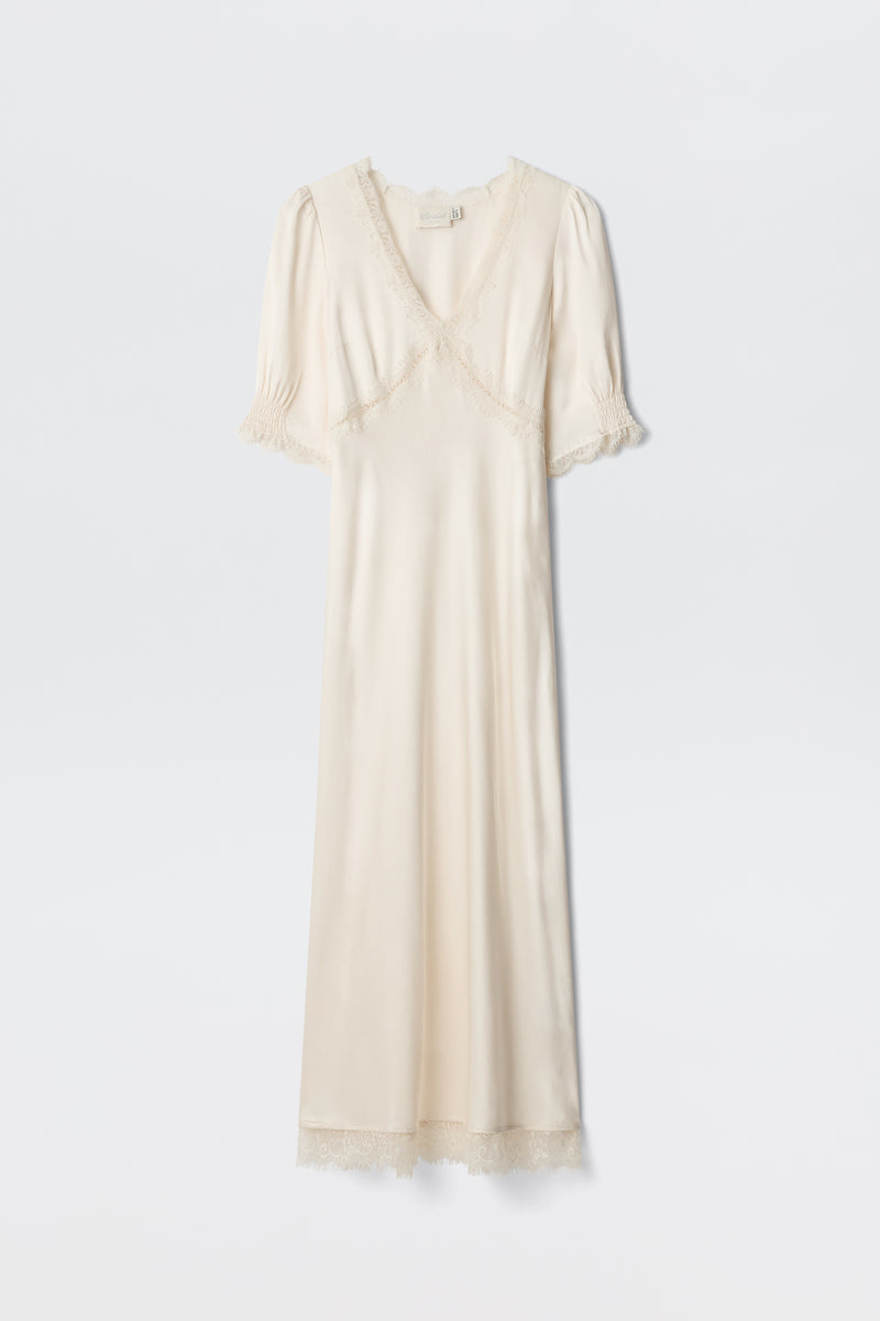 The Annina - Pearl is a cream satin dress with short puff sleeves, lace-trimmed neckline, sleeves, and hem, plus a subtle v-neckline. This vintage-inspired piece exudes elegant charm.