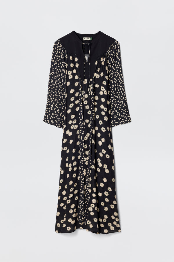 The Anela - Daisy Mix Black is a long-sleeved, lightweight black crepe boho dress with a cream floral print, V-neckline with ties, and a loose, flowy silhouette—perfect for everyday wear against a plain white background.