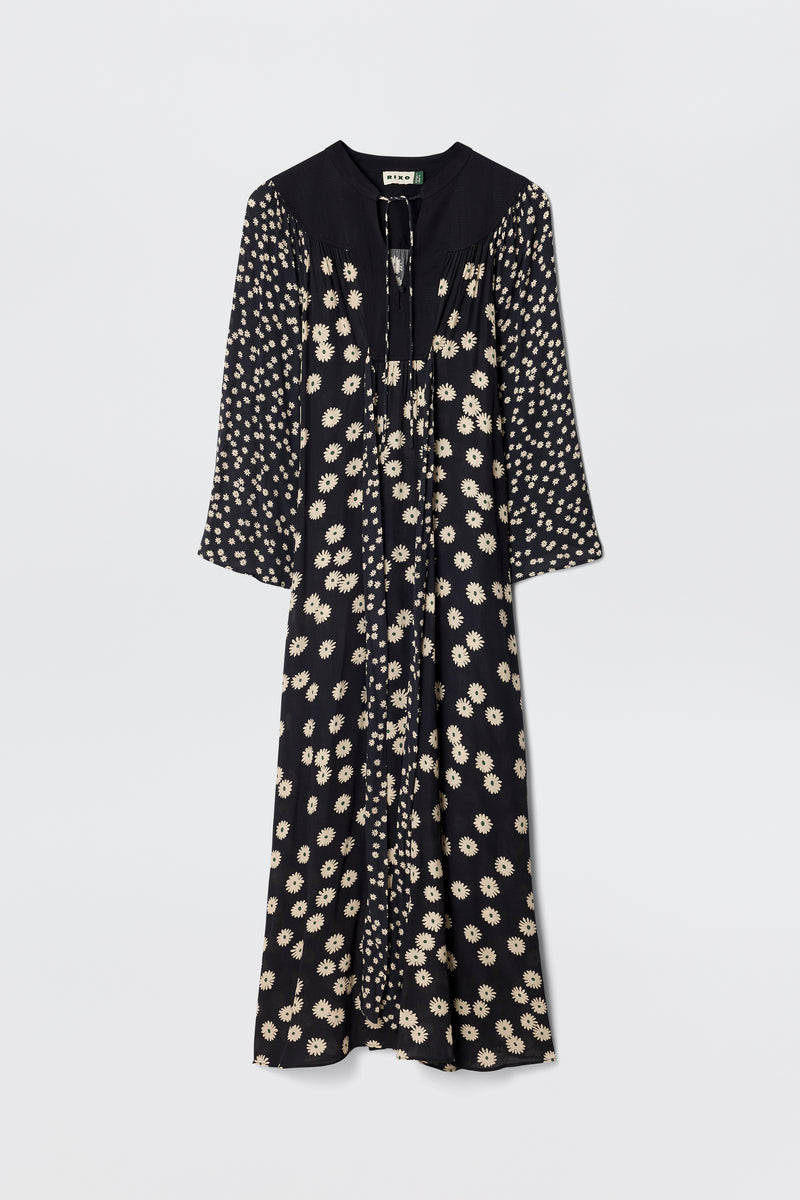 The Anela - Daisy Mix Black is a long-sleeved, lightweight black crepe boho dress with a cream floral print, V-neckline with ties, and a loose, flowy silhouette—perfect for everyday wear against a plain white background.