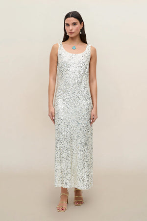 A woman stands facing forward against a plain beige background, wearing the Bondi - Mia Squiggle Embellishment Ivory dress. The sleeveless, ankle-length party dress features intricate embellishments. She has straight, dark hair and pairs the look with strappy sandals and minimal jewelry.