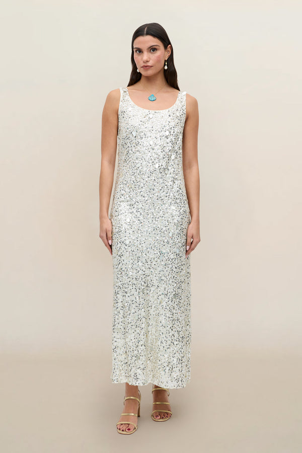 A woman stands facing forward against a plain beige background, wearing the Bondi - Mia Squiggle Embellishment Ivory dress. The sleeveless, ankle-length party dress features intricate embellishments. She has straight, dark hair and pairs the look with strappy sandals and minimal jewelry.