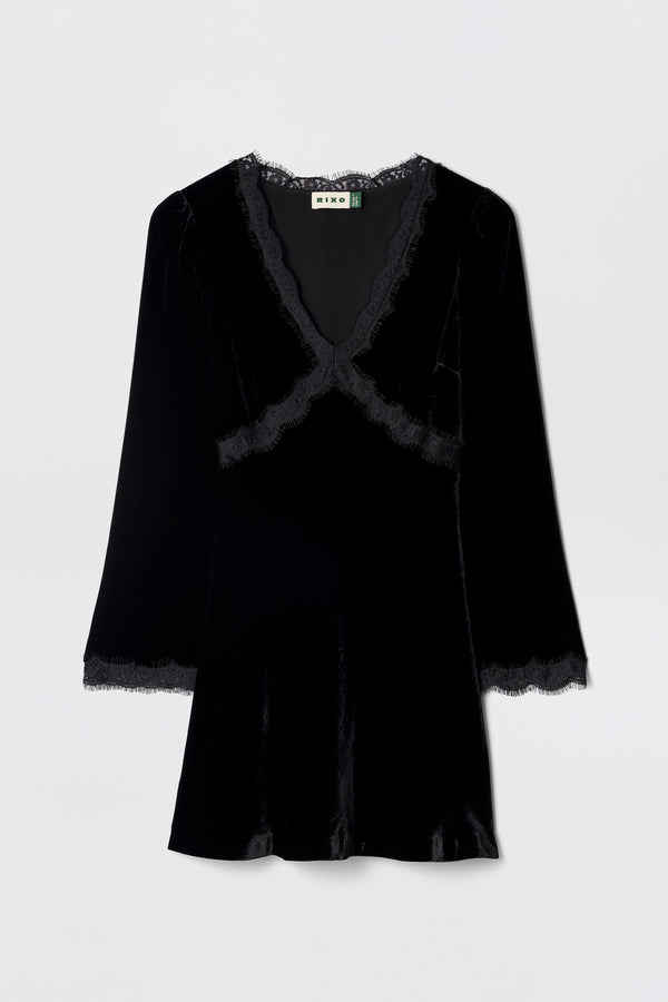The Macie - Black dress is a velvet little black dress with long sleeves, a V-neckline, and lace trim at the neckline, cuffs, and hem, shown against a plain light background.