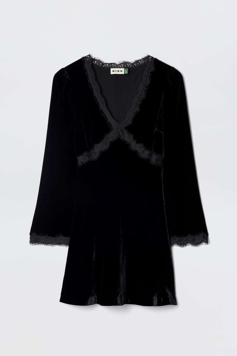 The Macie - Black dress is a velvet little black dress with long sleeves, a V-neckline, and lace trim at the neckline, cuffs, and hem, shown against a plain light background.