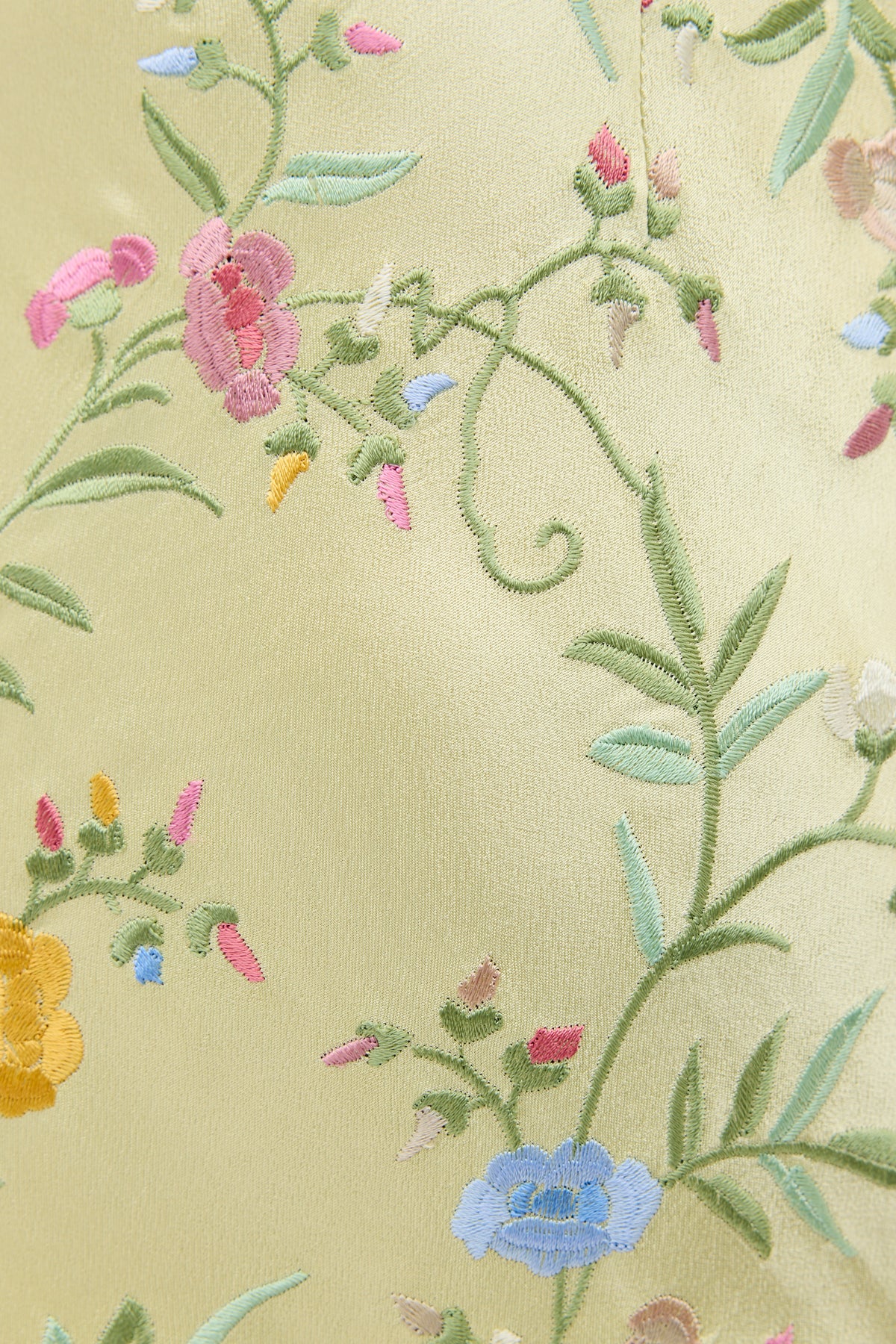 Close-up of Dune - Botanical Embroidery Green: pale yellow satin gown fabric featuring embroidered flowers and winding stems in pink, blue, yellow, and green—ideal for an elegant black tie dress.