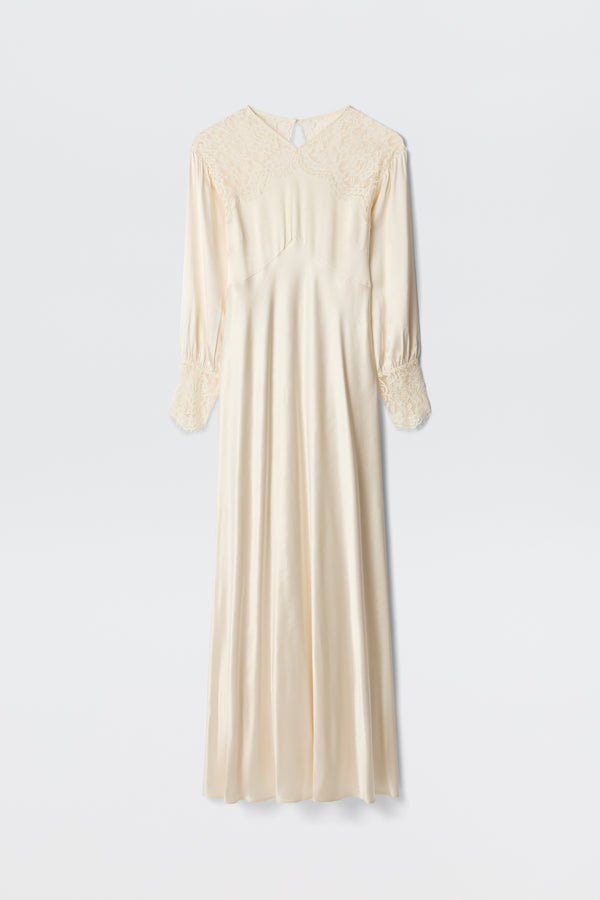 The Axelle - Pearl is an elegant long ivory satin dress featuring lace details on the shoulders and cuffs, long sleeves, and a loose, flowing silhouette. Photographed against a plain white background.