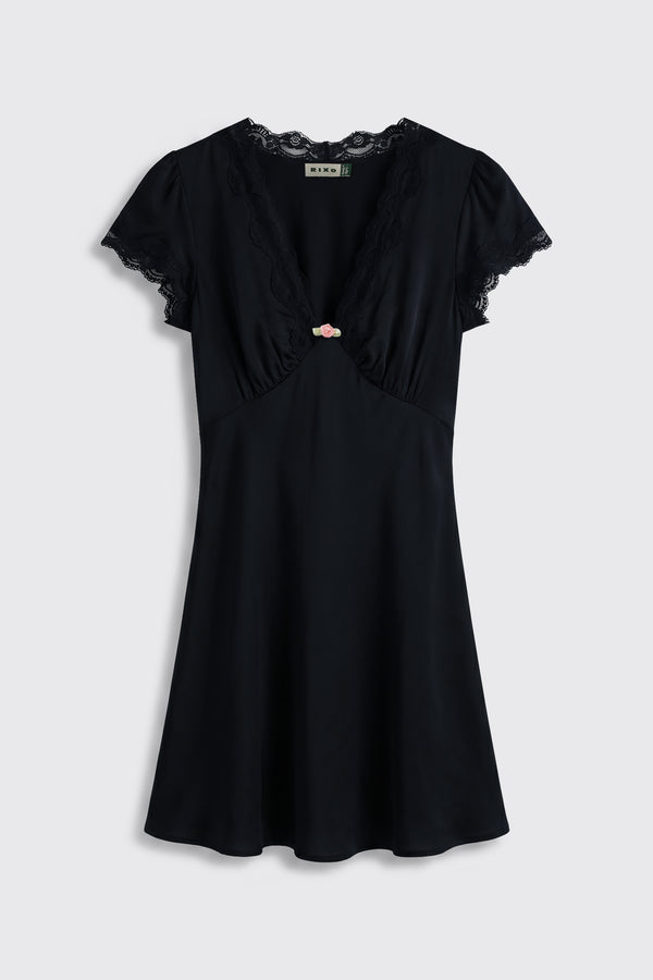 Cely - Black: A short-sleeved black dress featuring lace trim at the neckline and sleeves, a V-shaped front, and a small pink bow accent centered on the chest, showcased against a plain light background.