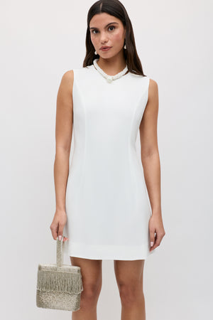 Woman in a sleeveless ivory mini dress (Katrin - Ivory) holding a textured silver fringe handbag and wearing a pearl necklace, standing against a plain light background—a perfect modern bridal look with elegant detailing.