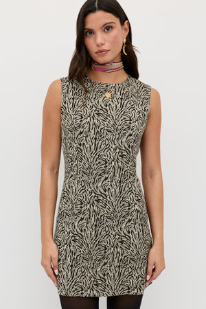 A woman with long brown hair wears the Katrin - Sun Leo Tan sleeveless, knee-length zebra print dress, accessorized with colorful layered necklaces and gold earrings, standing against a plain white background.