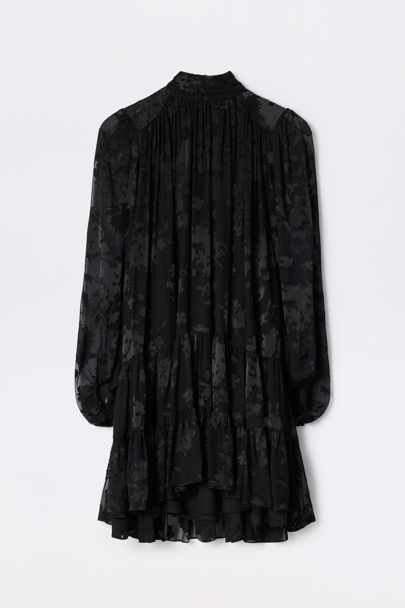 Anaya - Bouquet Devoré Black: Elegant, long-sleeve black dress featuring a floral devoré pattern, ruffled hem, and gathered back details, shown against a plain white background.