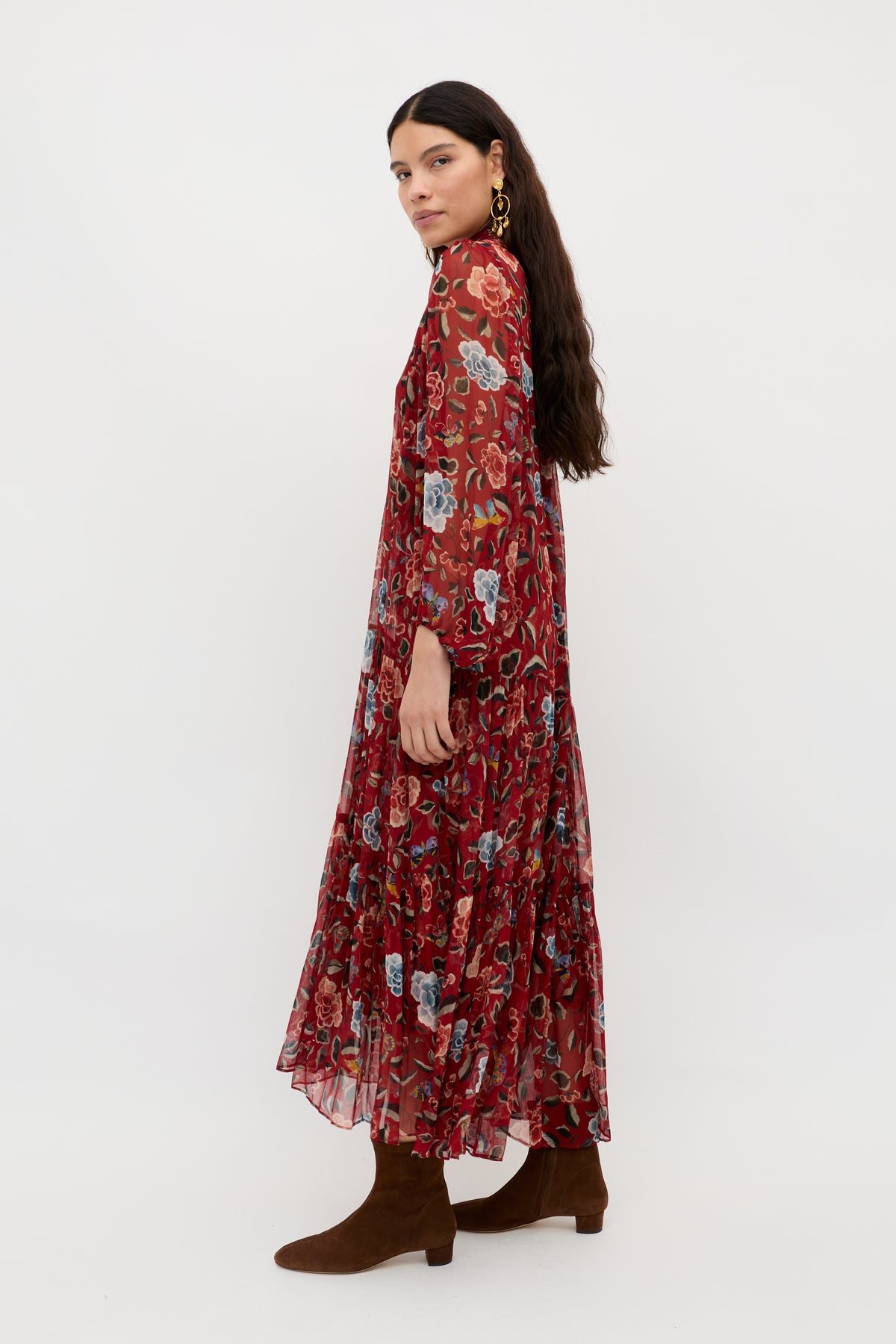 Woman with long, dark hair wearing the Adalind - Butterfly Floral Burgundy dress and brown ankle boots, standing sideways against a plain white background.
