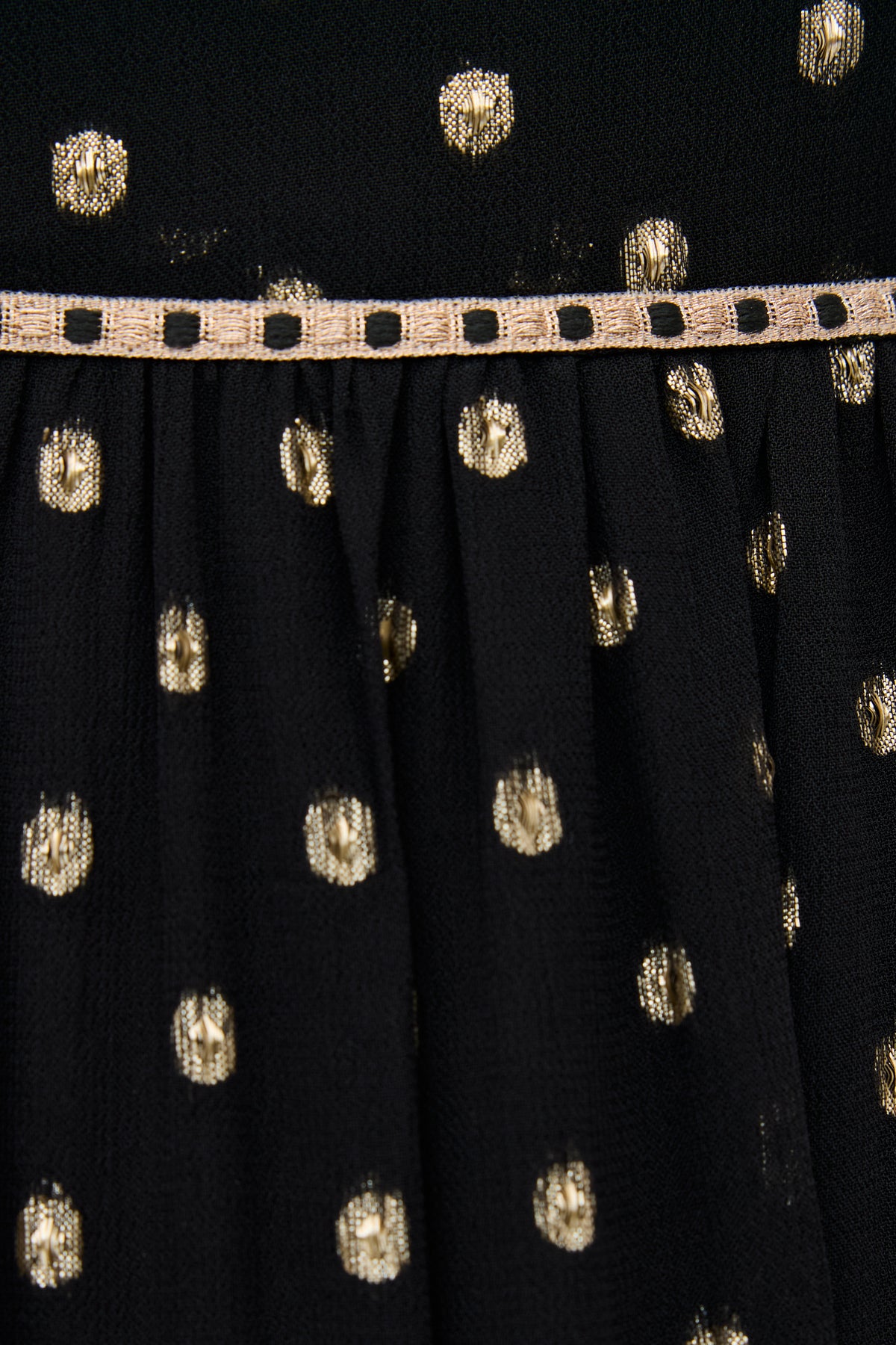 Close-up of Kamilah - Black fabric with gold polka dots, featuring a decorative beige ribbon with square cutouts running horizontally across the middle.