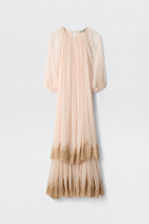 The Hayden - Shell is a long, sheer dress in pale pink with loose sleeves and a gathered neckline. Tan lace trim accents the hem and sleeve cuffs, while its flowing, lightweight design gives it a delicate and elegant style.