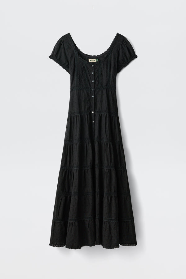 The Jaclyn - Black is an ankle-length, short-sleeve dress with a scoop neckline, button-down front, fitted bodice, flared tiered skirt, and subtle texture details. Shown against a plain white background.