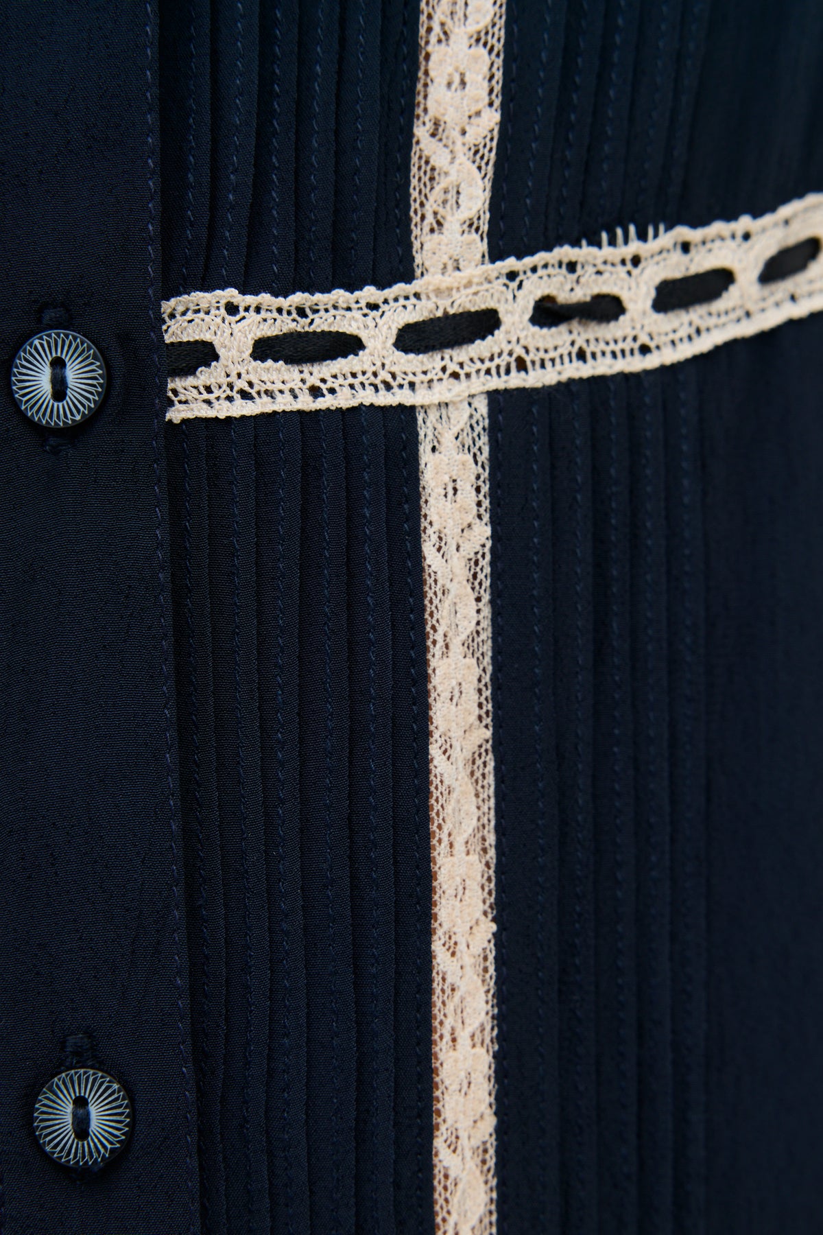 Close-up of the Kendara - Deep Navy dress, a cotton midi with vertical pleats, cream lace trim, and black buttons along the left side for a prairie-inspired look.