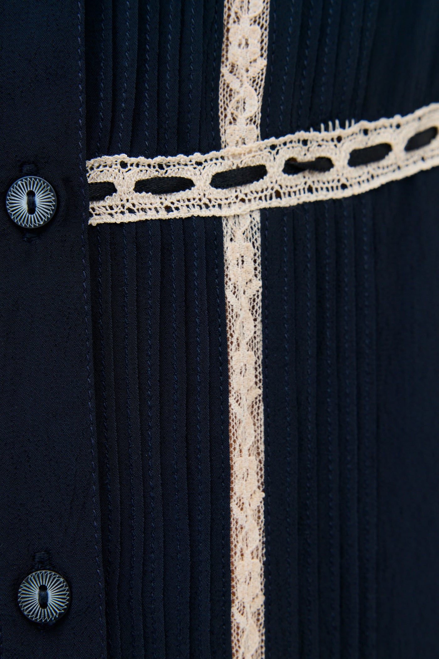 Close-up of the Kendara - Deep Navy dress, a cotton midi with vertical pleats, cream lace trim, and black buttons along the left side for a prairie-inspired look.