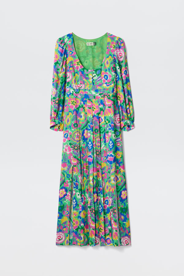 The Alfie - Ikat Bloom Green is a long, flowy dress with long sleeves, a V-neck, and pleats. It features a vibrant retro-inspired floral print in green, pink, blue, and yellow.