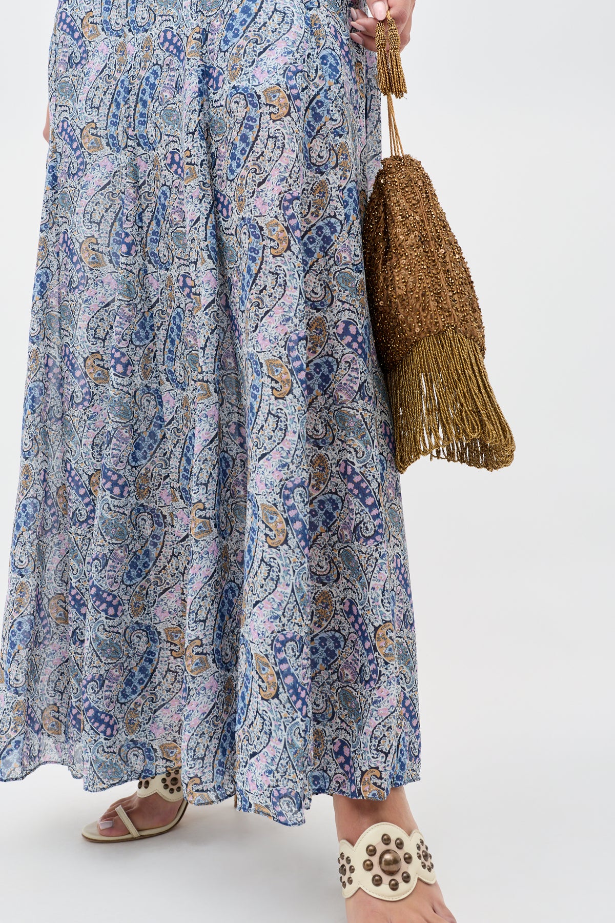 A person showcases the Orla - Vintage Scatter Embellishment Gold skirt, paired with studded white sandals and a brown fringed bag. Only the lower half of the body is visible against a plain background.