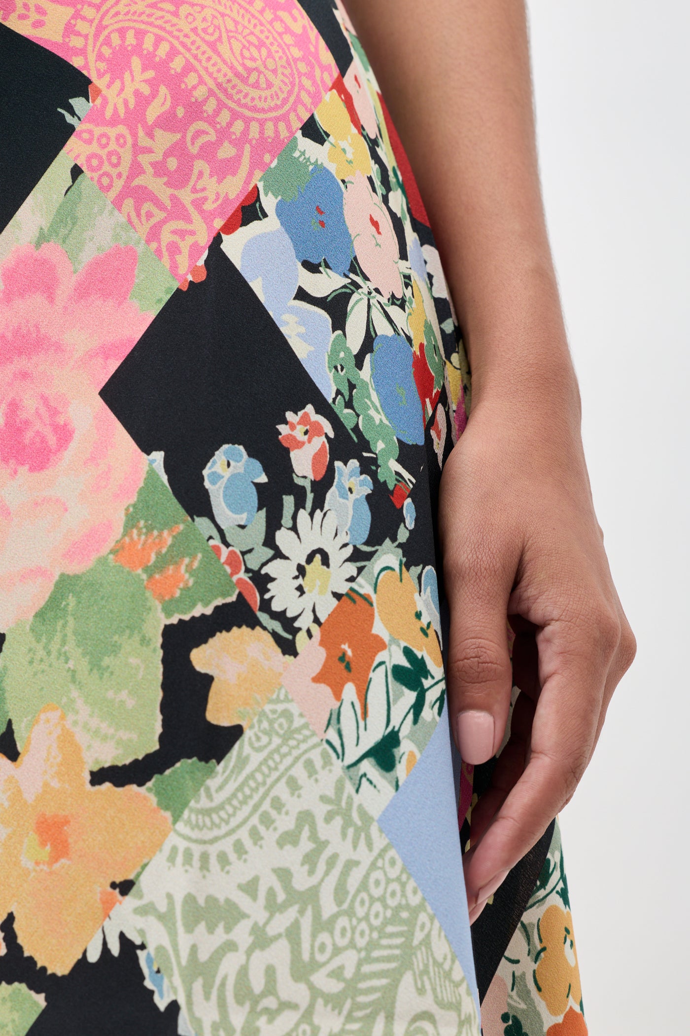 A close-up of a person's hand resting on the Adele - Olivia Patchwork Multi skirt, featuring an array of colorful floral and geometric designs.