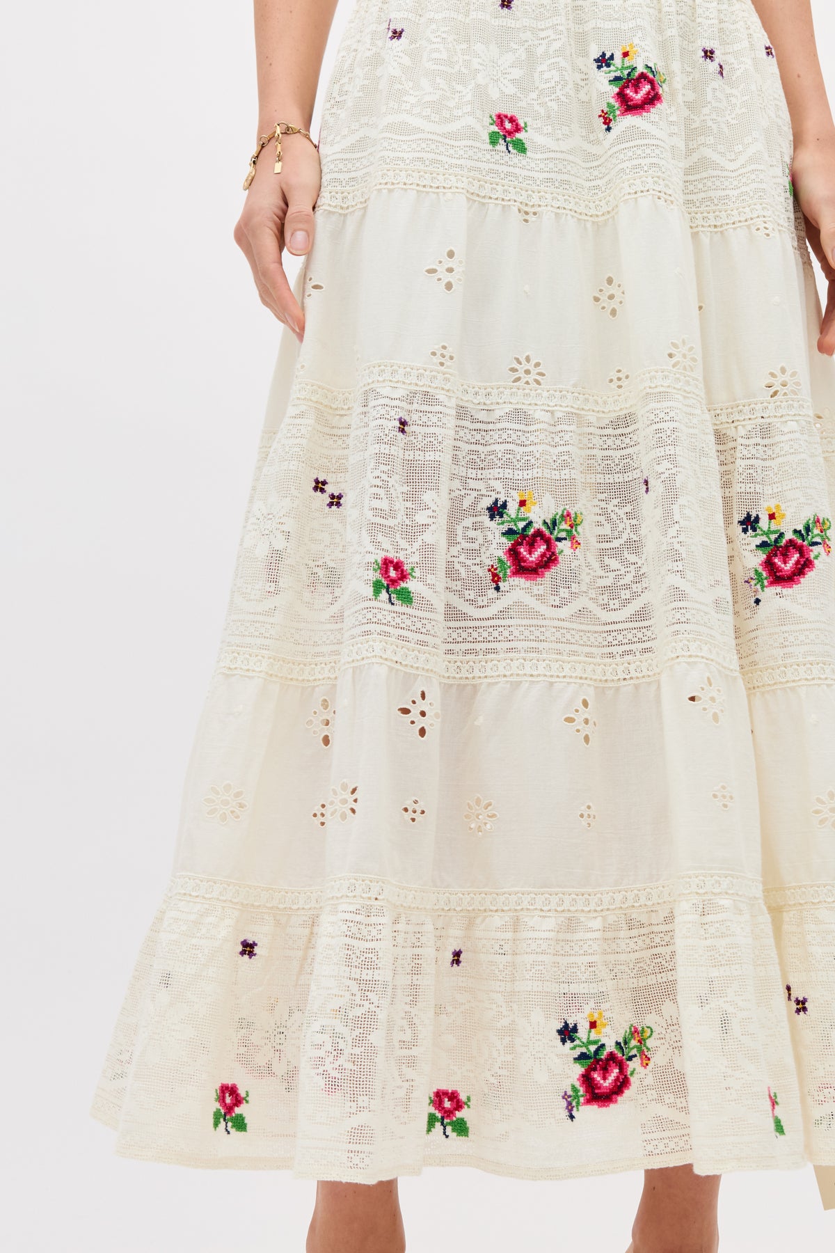 A close-up of the Cady - Spring Rose Embroidery Cream skirt, featuring cream lace with red, purple, and green floral embroidery, tiered sections, and part of a woman's arm and hand visible.