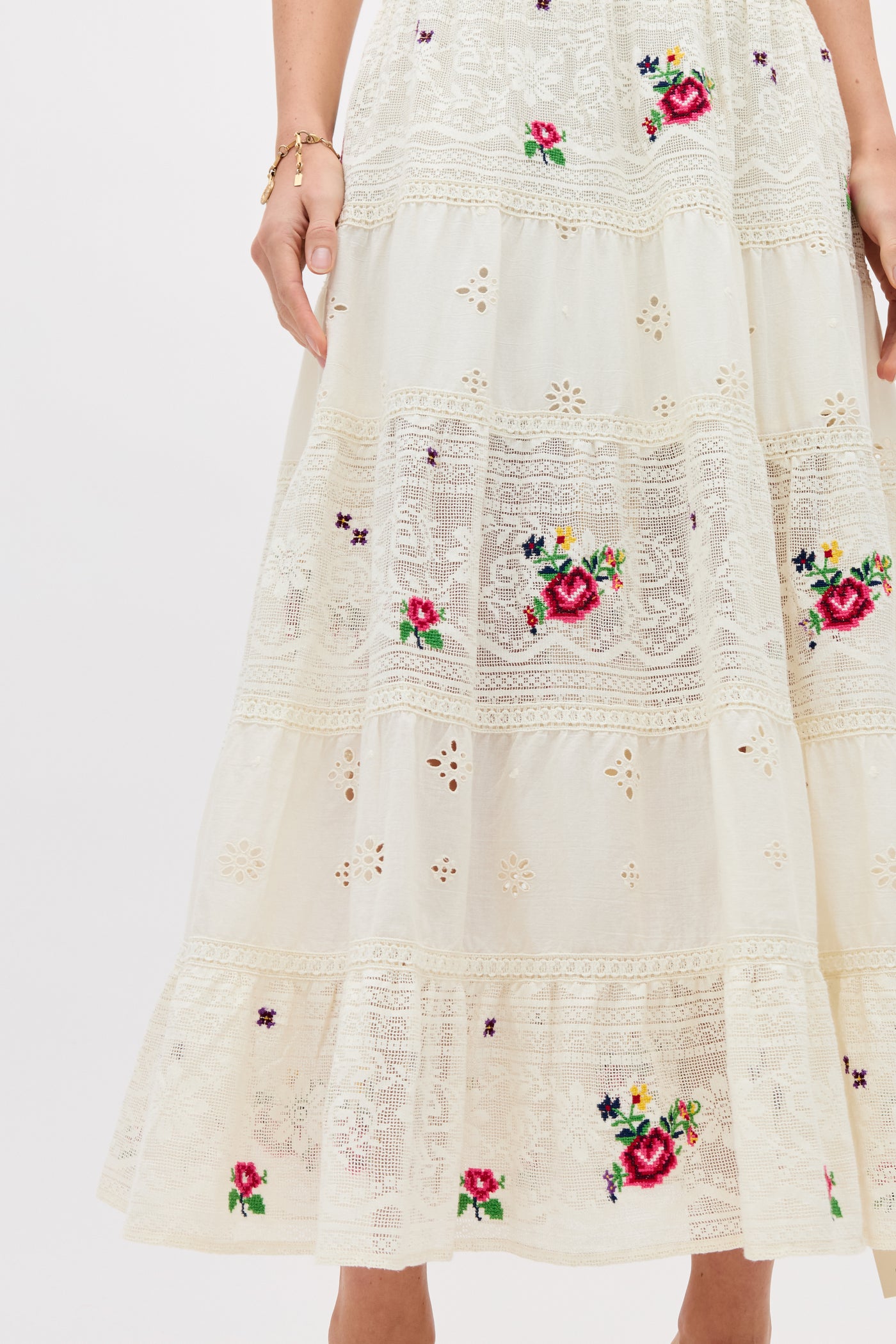 A close-up of the Cady - Spring Rose Embroidery Cream skirt, featuring cream lace with red, purple, and green floral embroidery, tiered sections, and part of a woman's arm and hand visible.