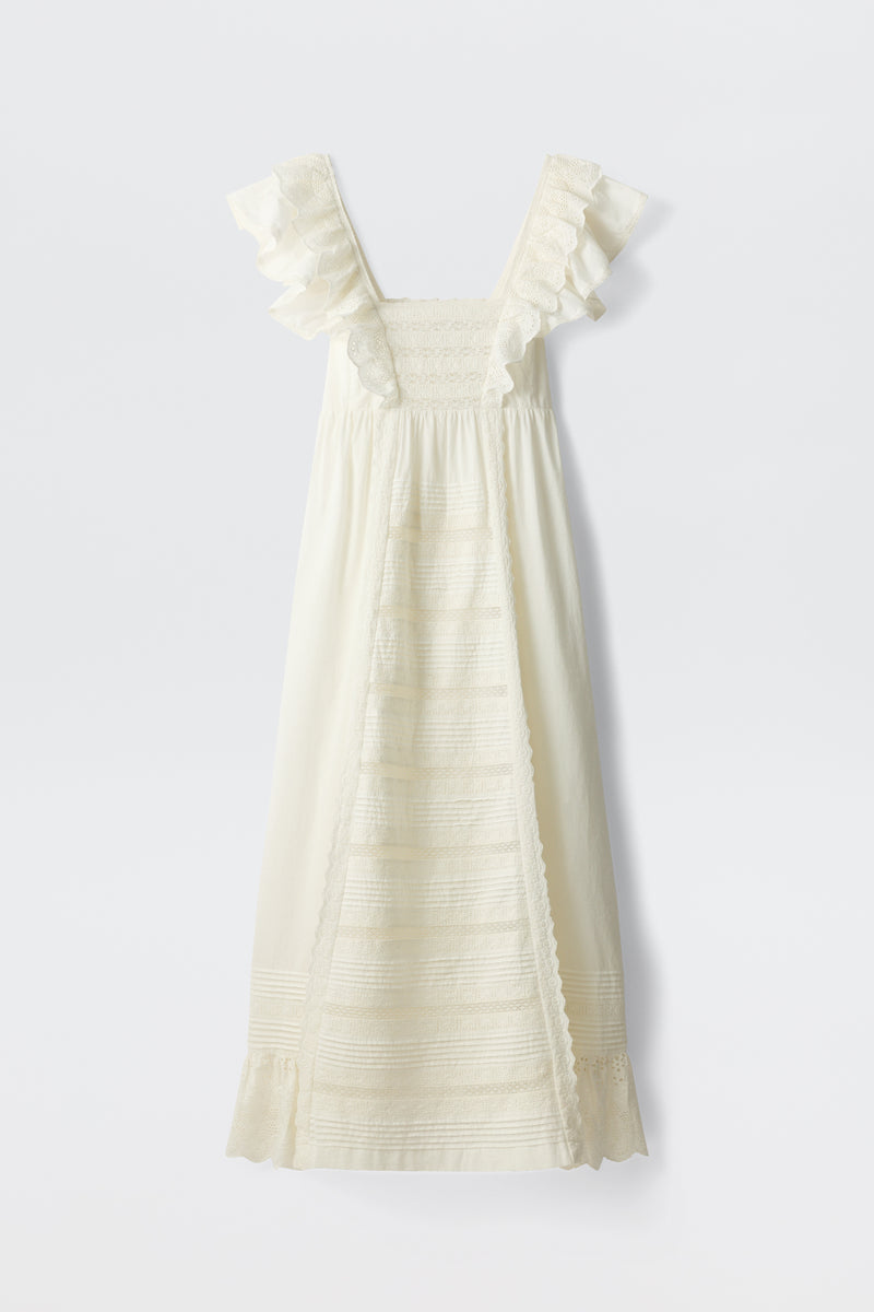 Delaney - White: A sleeveless, ivory-colored dress featuring ruffled shoulder straps, a smocked bodice, and lace detailing on the front panel and hem, displayed against a white background.