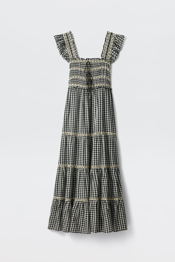 The Chandra - Beth Check Black is a sleeveless, ankle-length dress featuring a black and white gingham pattern, square neckline, ruffled straps, tiered skirt with lace trim on each tier, and vintage cottagecore style.