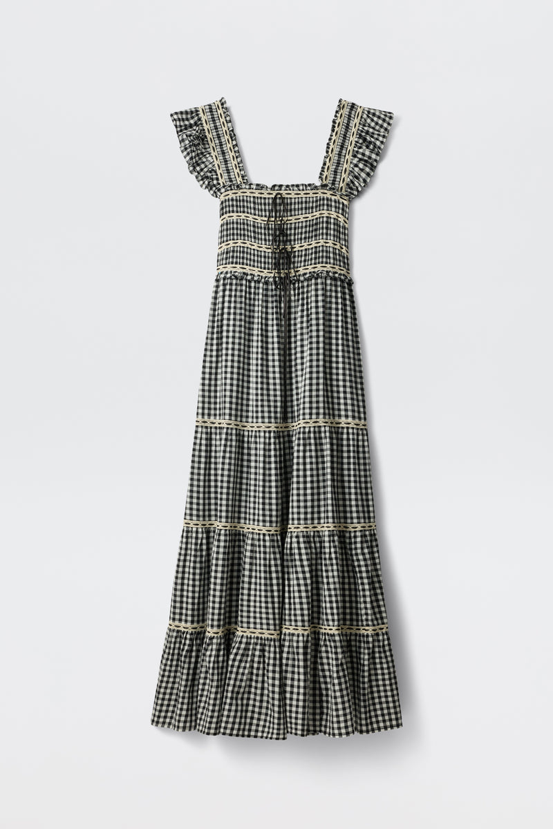 The Chandra - Beth Check Black is a sleeveless, ankle-length dress featuring a black and white gingham pattern, square neckline, ruffled straps, tiered skirt with lace trim on each tier, and vintage cottagecore style.