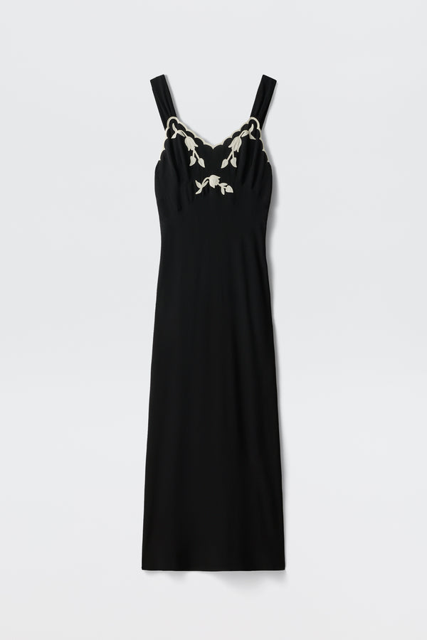 Julietta - Tulipa Appliqué Black: A sleeveless black midi dress with wide straps and a fitted silhouette, featuring white tulip appliqué at the neckline. Shown laid flat on a white background.