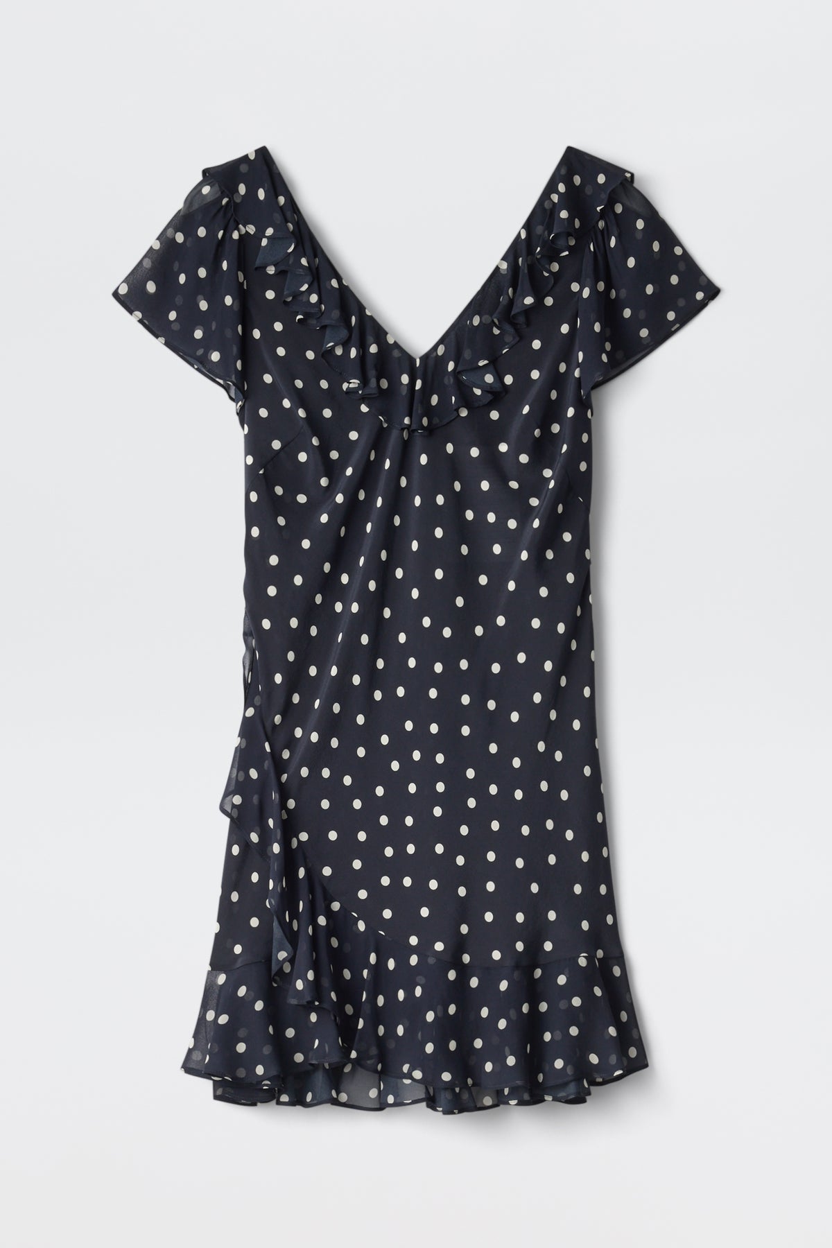 The Tally - Layla Dot Navy is a short-sleeved, navy blue dress with white polka dots, a V-neckline, ruffle details on the neckline and hem, and a slightly flared above-the-knee skirt.
