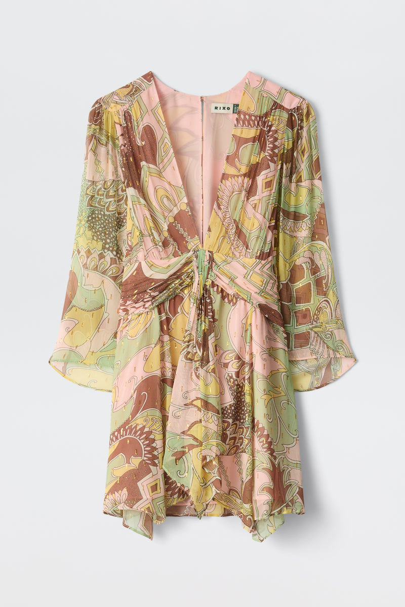 The Clove - Bianca Abstract Green is a flowy, V-neck mini dress with long sleeves, a front tie detail, and a loose fit. It features a colorful abstract pattern in pink, yellow, green, and brown.