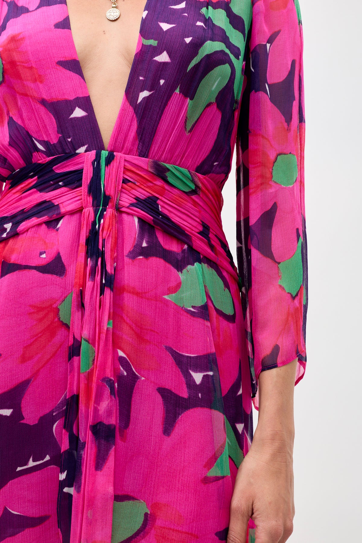 Someone wearing the Clove - Danish Floral Pink dress, which has a deep V-neckline, long sleeves, ruched waist, and vibrant pink, purple, green, and red floral patterns. Only the torso and part of one arm are visible.
