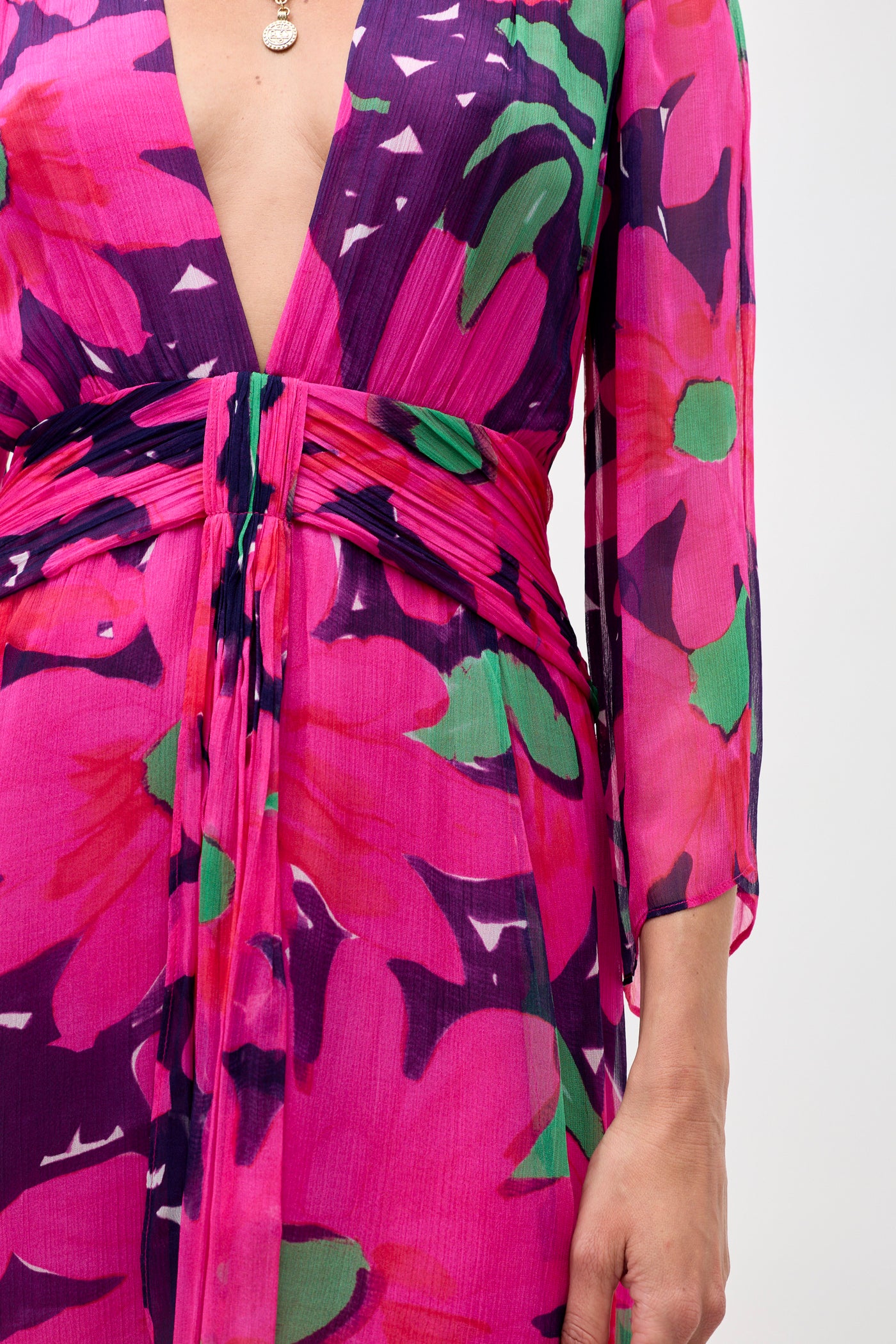 Someone wearing the Clove - Danish Floral Pink dress, which has a deep V-neckline, long sleeves, ruched waist, and vibrant pink, purple, green, and red floral patterns. Only the torso and part of one arm are visible.