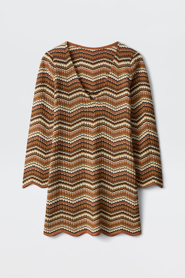The Ivia - Maria Chevron Brown top is a long-sleeve V-neck with wavy brown, cream, and black stripes. It features scalloped hems on the sleeves and edge, shown laid flat against a white background.