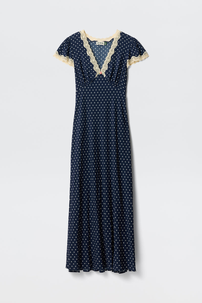 Clarice - Navy Polka Dot: A vintage-inspired, full-length rayon dress with white polka dots, short sleeves, and light beige lace trim on the V-neckline and sleeves, shown on a plain white background.